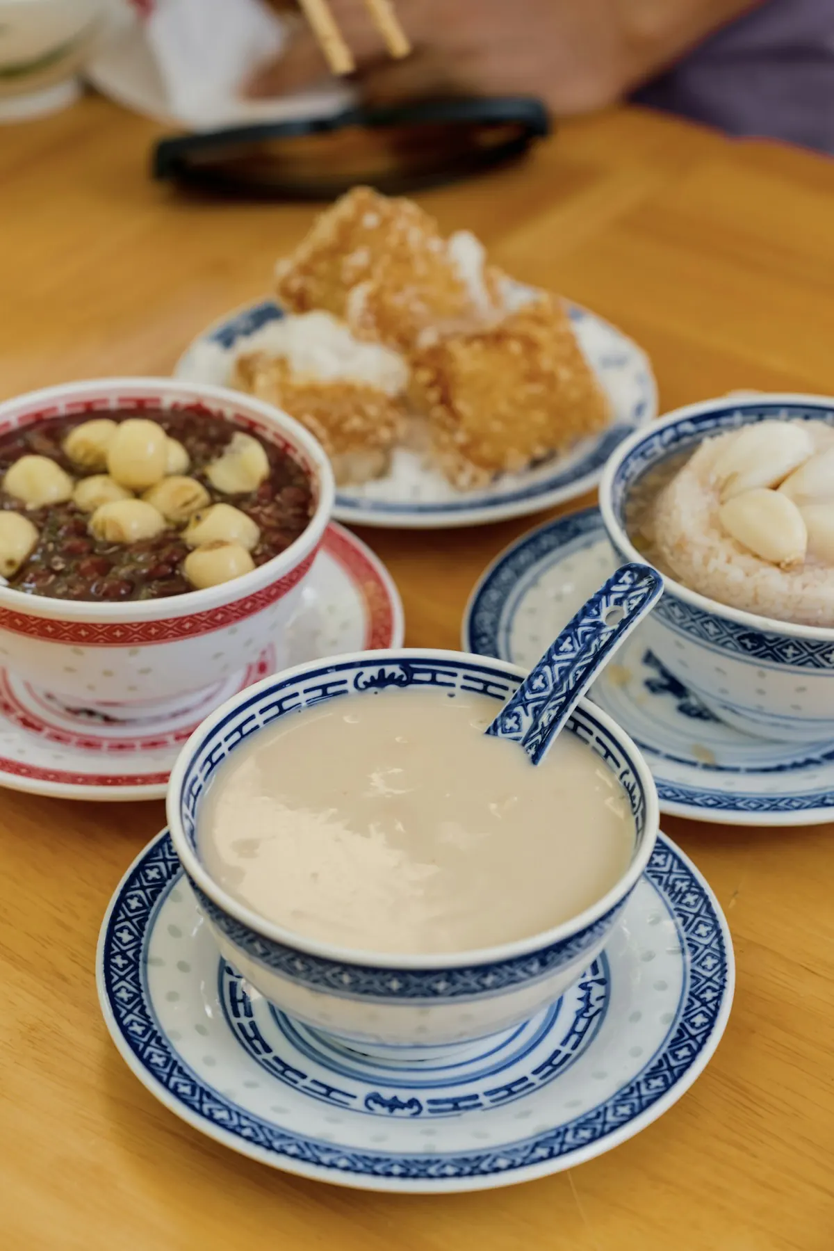 Blue-and-white bowls of sweet soup beside a plate of fried snacks on a wooden table